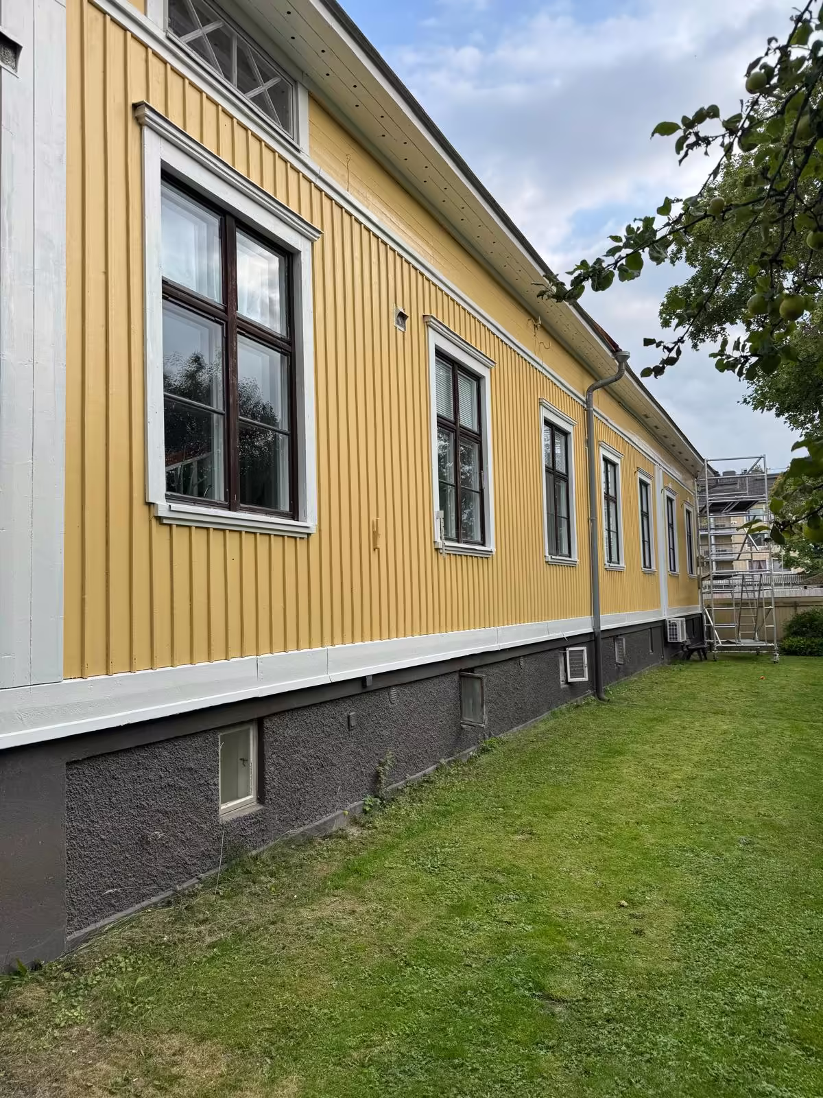 Sama sivuseinä maalauksen jälkeen, keltainen julkisivu, valkoiset ikkunanpielet ja maalattu sokkeli
