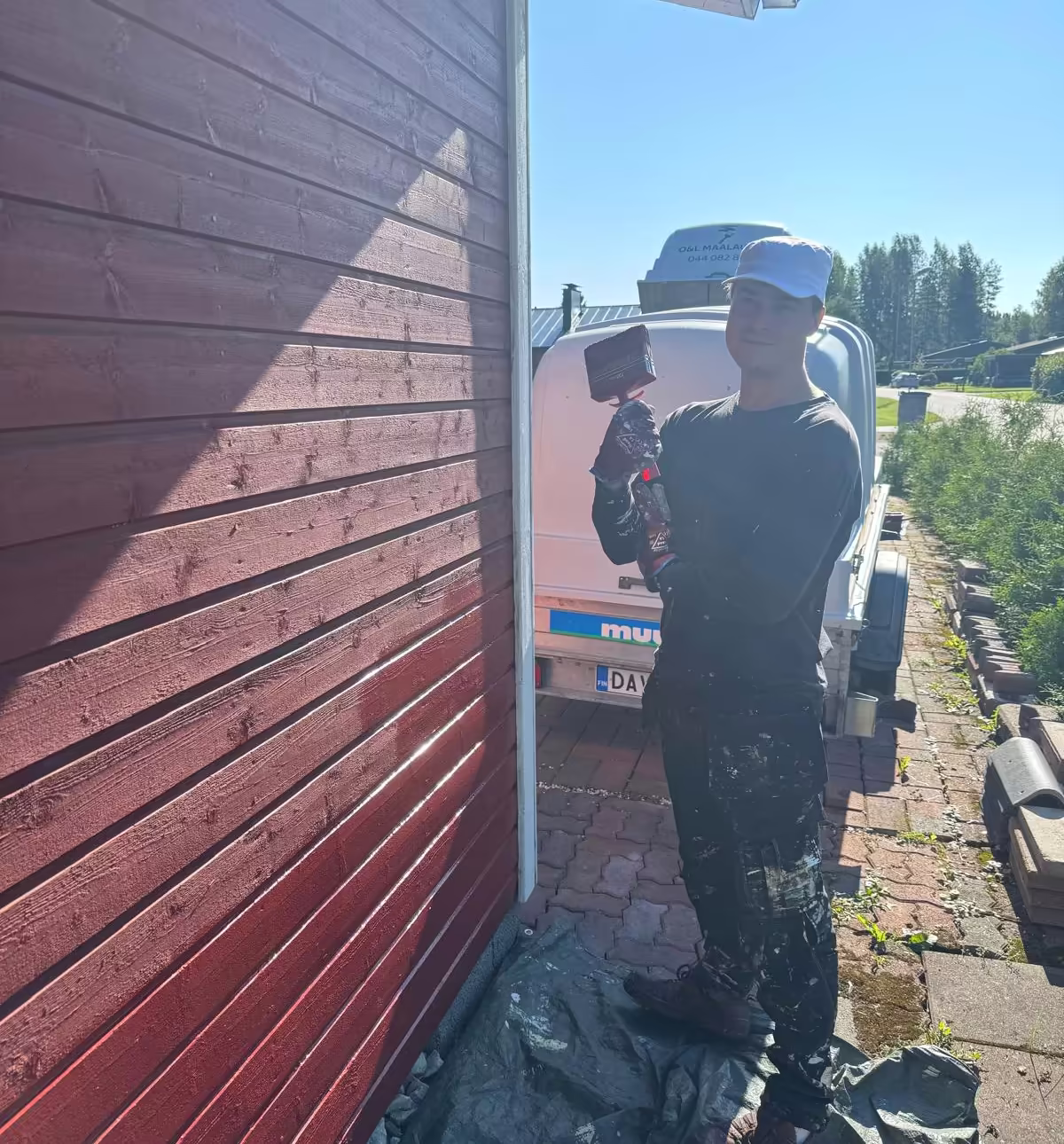 Maalari maalaa punaisen puutalon lautaverhoilua telinettä vasten