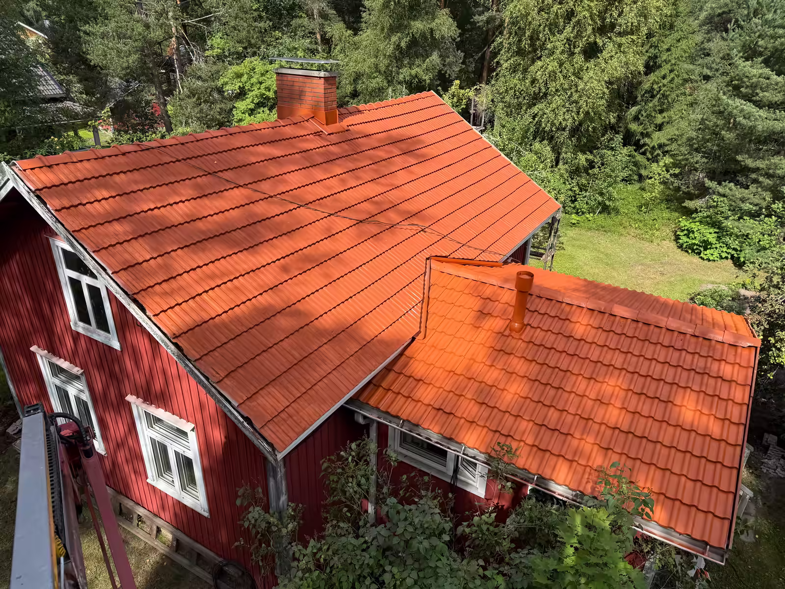 Tiilenpunaiseksi pinnoitettu tiilikatto punaisessa puutalossa ylhäältä kuvattuna
